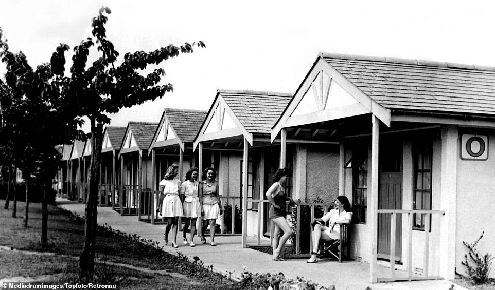 A typical cabin pictured set up in an early Butlin's holiday camp, with two holidaymakers pictured chatting outside one of the affordable accommodations while three others walk past nearby