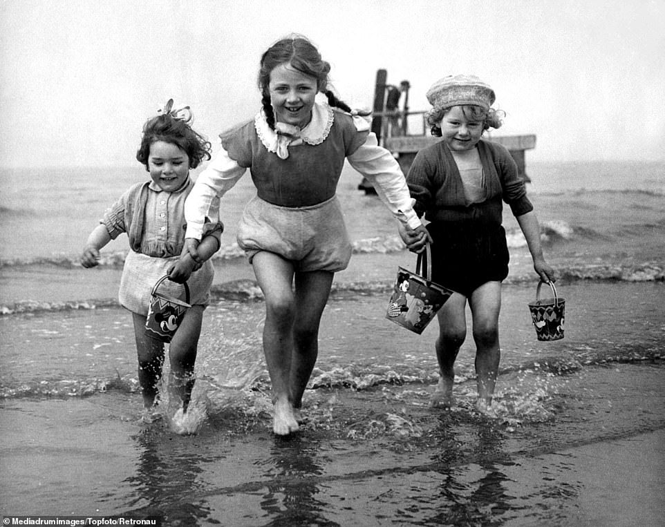Three beaming children come out of the sea while holding buckets on their Butlin's holiday. The camps boasted a host of decidedly modern features in the 60s, introducing the famous monorails and glass-sided swimming pools